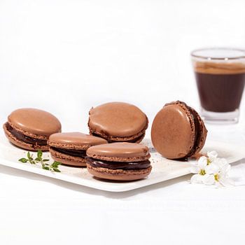Homemade chocolate macarons on a white plate and a cup of expresso