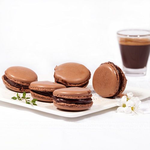 Hausgemachte Schokoladen-Macarons auf einem weißen Teller und eine Tasse Expresso