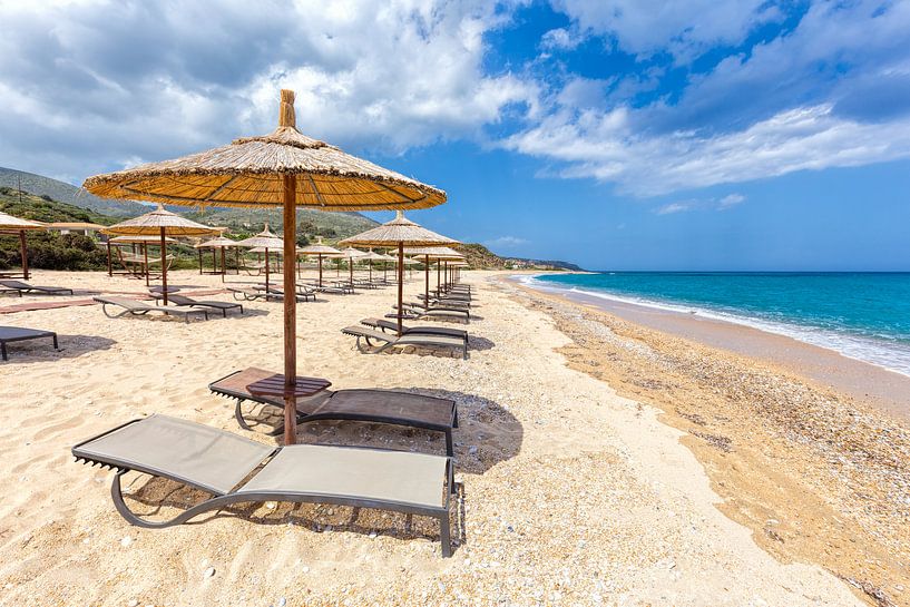 Beach umbrellas in rows on sandy beach with sea by Ben Schonewille