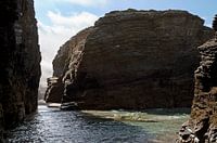 The sun shines through rock formations on the beach at Playa de las Catedrales in Galicia, Spain