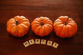 three pumpkins in a row with the word autumn in scrabble letters by Margriet Hulsker
