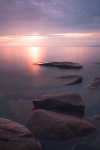 Les pierres s'éloignent sous l'eau rose du coucher de soleil du lac Baïkal, photo verticale