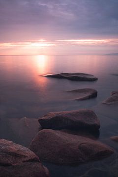 De stenen gaan de verte in onder het roze ondergaande water van het Baikalmeer, verticale foto