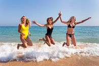 Drie meisjes springen op strand bij zee van Ben Schonewille thumbnail