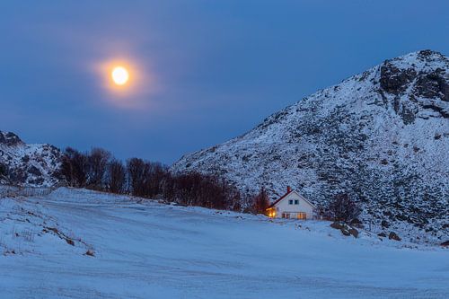 Haus mit gemütlichem Licht an einem verschneiten Berghang bei Vollmond