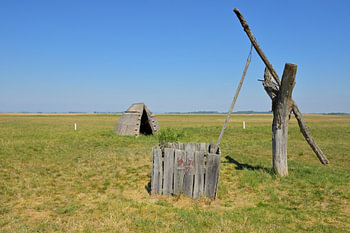 An old draw well and a reed hut beneath a clear blue sky