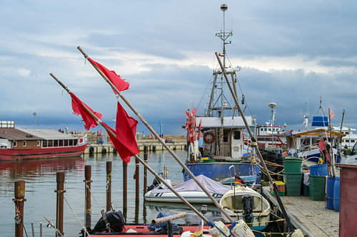 Rote Fahnen und Fischerboote am Hafen von Sassnitz auf der Insel Rügen in der Ostsee vor bewölktem H