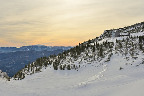 Paysage hivernal avec un refuge de montagne et un ciel teinté par la poussière du Sahara