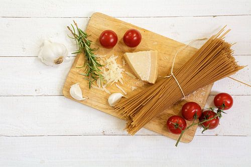 kitchen board with ingredients for an Italian meal seen from above with wholemeal spaghetti, tomato, by Maren Winter
