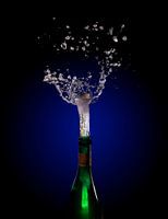 Champagnerflaschenexplosion mit korkspringendem Spritzer vor einem dunklen Hintergrund mit blauem bi