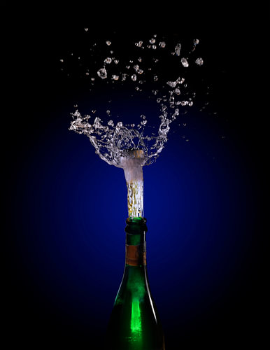 Champagnerflaschenexplosion mit korkspringendem Spritzer vor einem dunklen Hintergrund mit blauem bi