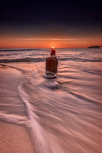The sea washes around the groyne as the sun rises on the horizon