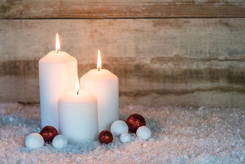 Three Christmas candles with red and white ornaments on snow by Alex Winter