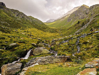 Alpine Valley and Mountain Stream Leading to a Misty Pass in Italy