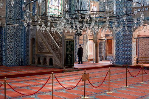 Man in gebed, Moskee in Istanbul, Turkije, met prachtige blauwe tegels en rood tapijt.