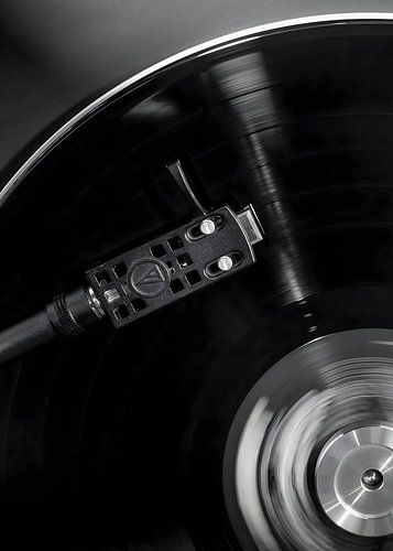 Monochrome close up of a turntable tonearm on a spinning vinyl record Monochrome close up of a turntable tonearm on a spinning vinyl record
