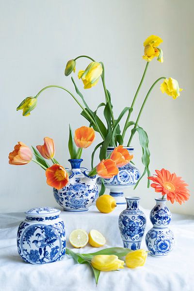 Uitbundig stilleven met tulp,citroen, gerbera in  delfts blauwe vaasjes lichte achtergrond van Leoniek van der Vliet