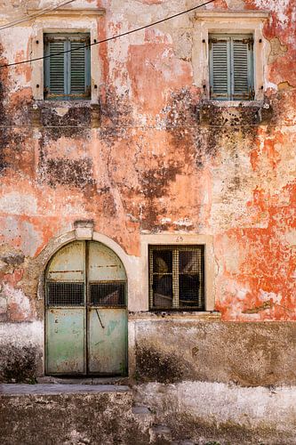 Maison aux murs rouges patinés, avec des portes, des fenêtres et des volets