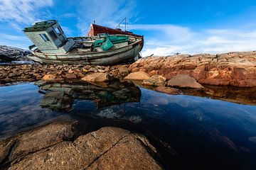 Shipwreck on the rocks reflects in the water by Martijn Smeets