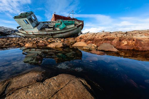 Shipwreck on the rocks reflects in the water