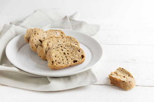 frisches Vollkornbrot auf einem Teller, auf einem weiß gestrichenen rustikalen Holztisch, Kopierraum