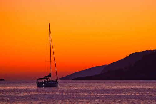 sailing yacht parked in the warm tropical sea under a bright orange sunset, relaxation and resort.