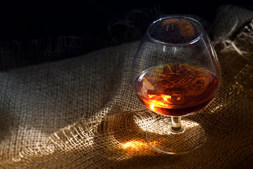 Cognac oder Brandy im Glas mit glühendem Lichtreflex auf rustikalem Sackleinen, Konzept für Genuss o