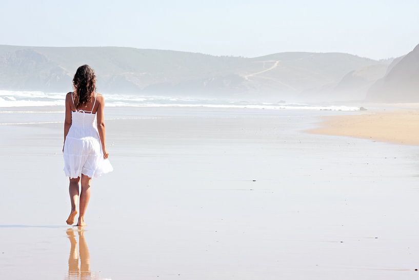 Jonge vrouw wandelt langs een verlaten strand van Eye on You