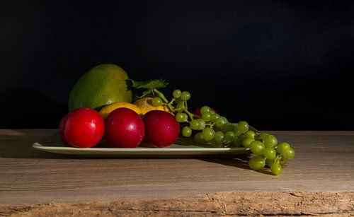 still life with a green bowl on a reflective background with mango,lemons,grapes and plums
