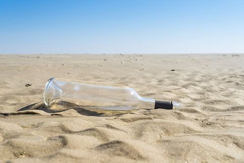 Een afval glas wijn fles op zand strand in de zon, concept van oceaan afval en vervuiling