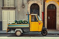 A yellow Piaggio Ape full of melons.