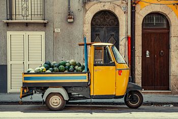 A yellow Piaggio Ape full of melons.