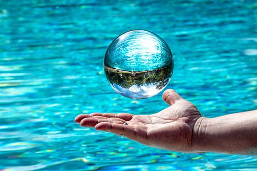 Glazen bal die over een hand voor de achtergrond van het water zweeft met gespiegelde bewolkte lucht