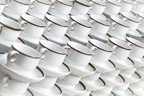 Witte koffiekopjes met bordstandaard op een rijtje gestapeld