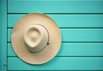 Strohhut an türkisfarbener Holzwand hängend von Markus Gann
