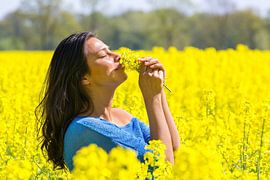 Woman smells beautiful flowers in yellow rapeseed field