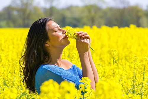 Vrouw ruikt aan bloemen in geel koolzaadveld