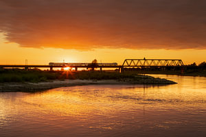 IJssel-Eisenbahnbrücke mit Zug bei Deventer in der goldenen Stunde