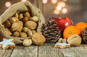 Kerstmaaltijd met noten in kerstmanzak, rode appel, oranje fruit en stervormig koekje van Alex Winter