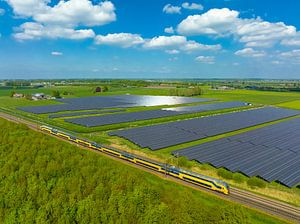 Ein Zug der niederländischen Eisenbahn fährt an einem Feld mit Solarzellen vorbei