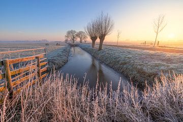 De eerste zonnestralen verlichten een klassiek Hollands polderlandschap tijdens zonsopkomst in de winter van Bas Meelker