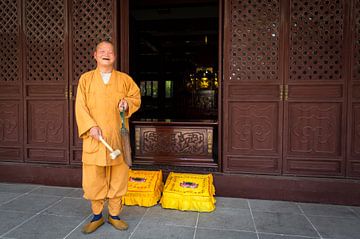 Lachende boeddhistische monnik slaat op een gong, China van Ger Beekes