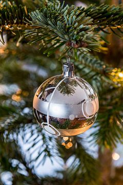 Zilverkleurige kerstbal en lichtjes in de kerstboom van Wim Stolwerk