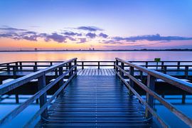 Een steiger aan een meer tijdens een rustige zonsopkomst van Eelco de Jong