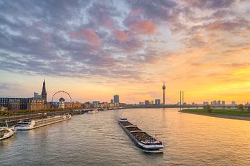 La ligne d'horizon de Düsseldorf avec un bateau sur le Rhin au coucher du soleil sur Michael Valjak
