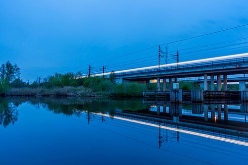 Streaks of light from a train on a railway bridge at dusk by Eugene Winthagen