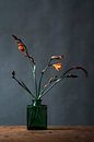 Foto print van oranje bloem in groene glazen vaas tegen een blauwe achtergrond van Jenneke Boeijink thumbnail