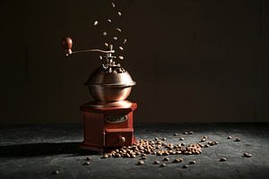 Houten vintage koffiemolen op een leisteenplaat, vallende en liggende gebrande bonen tegen een donke