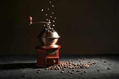 Wooden vintage coffee grinder on a slate plate, falling and lying roasted beans against a dark backg