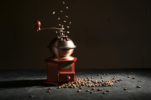 Hölzerne Vintage-Kaffeemühle auf einer Schieferplatte, fallende und liegende geröstete Bohnen vor du